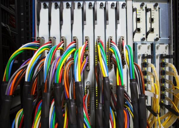 Fasci di cavi colorati con guaine nere collegati ai moduli di un armadio rack, accanto a cavi in fibra gialli